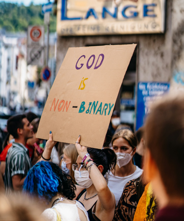 Aktivist med munnbind holder opp plakat med påskriften "God is non-binary" på en demonstrasjon