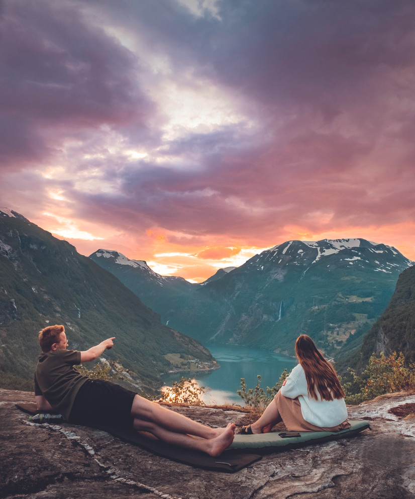Foto fra boka Tur-retur Norge av Helene Myhre Østervold. Viser et par som sitter med utsikt til fjord og fjelltopper.